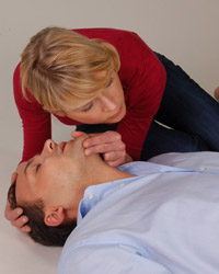 Foto: Eine Frau kontrolliert die Atmung bei einem Mann.